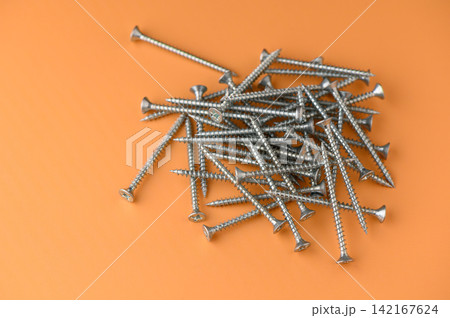 Collection of shiny silver screws scattered on a bright orange background, creating a vibrant contrast that highlights their detailed textures and shapes Collection of shiny silver screws scattered on a bright orange background, creating a vibrant contrast that highlights their detailed textures and shapes 142167624