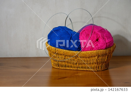 Basket filled with blue and pink yarn balls and circular knitting needles on a wooden table Basket filled with blue and pink yarn balls and circular knitting needles on a wooden table 142167633