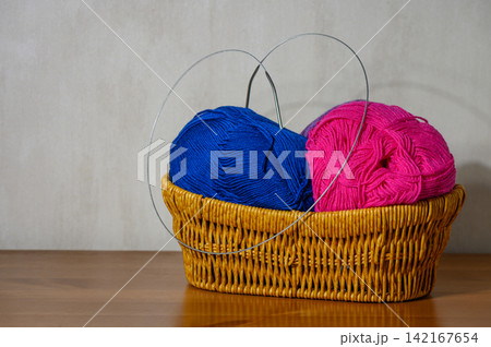 Wicker basket with vibrant magenta and sapphire yarn skeins and circular needles Wicker basket with vibrant magenta and sapphire yarn skeins and circular needles 142167654
