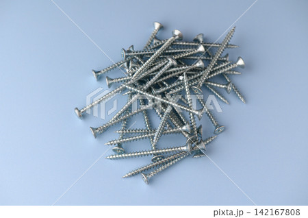 Scattered silver screws create a shiny landscape on a soft blue surface inviting creativity and craftsmanship Scattered silver screws create a shiny landscape on a soft blue surface inviting creativity and craftsmanship 142167808