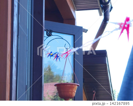 Clothesline with colorful plastic clips hanging outside a wooden house window. Household drying task and laundry chores. Domestic life scene with outdoor hanging plant and architecture. 142167895