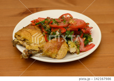 Roasted Chicken Pieces with Tomato Salad on a Wooden Table Roasted Chicken Pieces with Tomato Salad on a Wooden Table 142167986