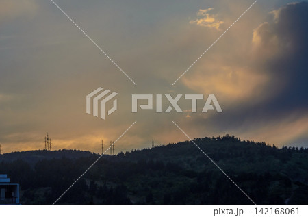 Golden hues dance across the evening sky over distant hills with power lines silhouetted against a dramatic backdrop Golden hues dance across the evening sky over distant hills with power lines silhouetted against a dramatic backdrop 142168061