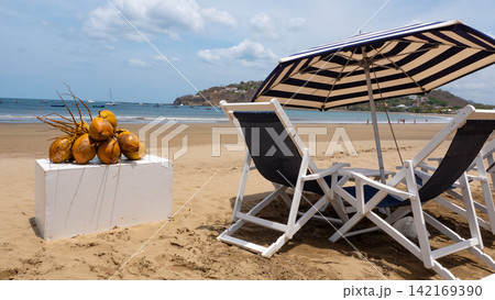 Sunbed at tropical beach with coconut. Beach sunbed with parasol and island food of coconut. Summer vibes. Vacation in summer. Luxury vacation. Coconut at beach sunbed. Summer vacation. Luxury life Sunbed at tropical beach with coconut. Beach sunbed with parasol and island food of coconut. Summer vibes. Vacation in summer. Luxury vacation. Coconut at beach sunbed. Summer vacation. Luxury life 142169390
