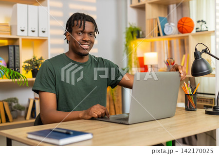 African American young man on home table opening laptop to start remote work in living room indoors African American young man on home table opening laptop to start remote work in living room indoors 142170025