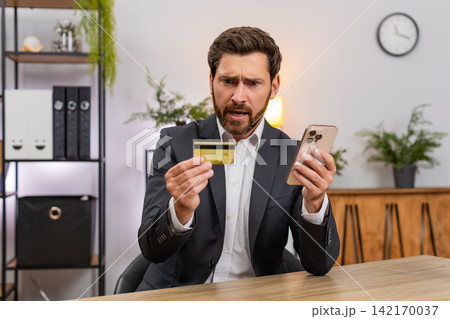Middle-aged businessman sighs at insufficient funds holding smartphone and credit card about balance Middle-aged businessman sighs at insufficient funds holding smartphone and credit card about balance 142170037