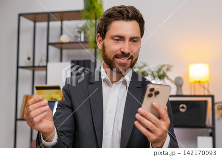 Middle-aged businessman pays corporate bill with credit card on smartphone nods happy after purchase Middle-aged businessman pays corporate bill with credit card on smartphone nods happy after purchase 142170093