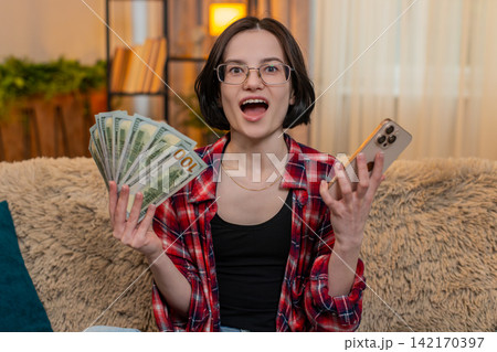 Young woman celebrating money win on smartphone raising arms after hitting jackpot in online lottery Young woman celebrating money win on smartphone raising arms after hitting jackpot in online lottery 142170397