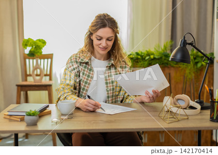 Young woman on home table compares two documents reads contract terms marks key point makes decision Young woman on home table compares two documents reads contract terms marks key point makes decision 142170414