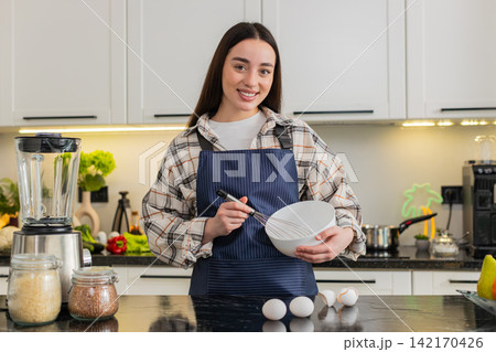 Young woman cracking eggs in kitchen bowl preparing simple breakfast omelet or baking dough at home 142170426