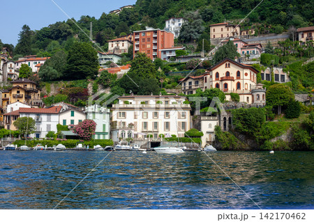 Multicolor houses building architecture on lake Como, Italy city on mountain. Boats on water waves Multicolor houses building architecture on lake Como, Italy city on mountain. Boats on water waves 142170462