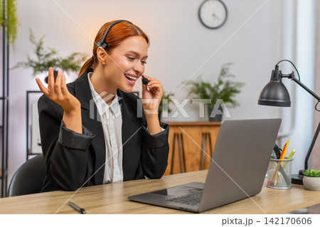 Young businesswoman in headset leads client video call on laptop smiling and speaking during support 142170606