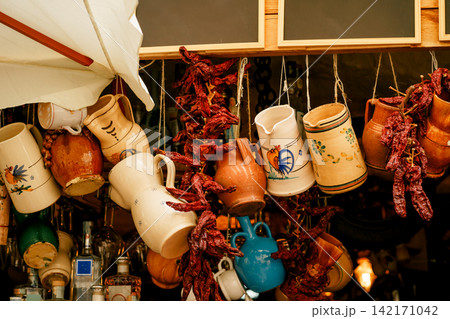 Traditional ceramic jugs and dried Capsicum annuum peppers decorate a Mediterranean market stall. Concept of heritage, cuisine, craftsmanship, travel Traditional ceramic jugs and dried Capsicum annuum peppers decorate a Mediterranean market stall. Concept of heritage, cuisine, craftsmanship, travel 142171042