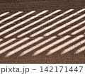 Diagonal light stripes creating abstract shadow pattern on textured ground 142171447