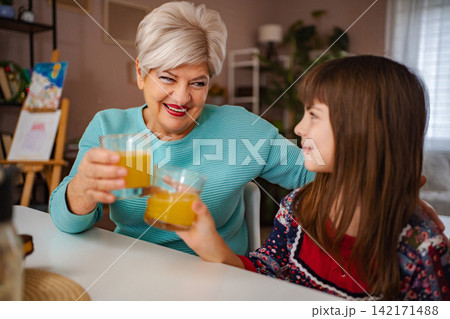 Grandmother and grandchild toasting with orange juice at home Grandmother and grandchild toasting with orange juice at home 142171488