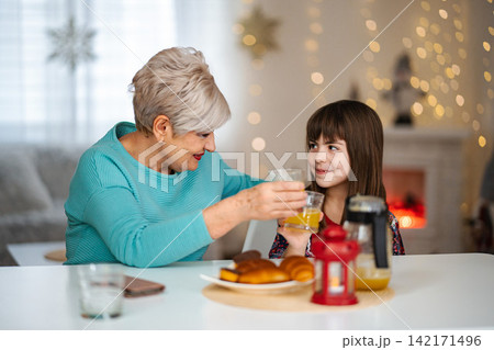 Grandmother and granddaughter enjoying festive breakfast with orange juice Grandmother and granddaughter enjoying festive breakfast with orange juice 142171496