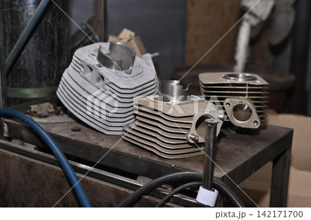 Disassembled motorcycle cylinder blocks lie on workshop table during repair. Disassembled motorcycle cylinder blocks lie on workshop table during repair. 142171700