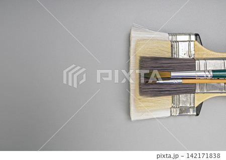 Various sizes of synthetic and natural bristle paintbrushes stacked on a neutral grey background for fine art painting, wall decorating, home renovation, and creative artistic craft hobby projects 142171838