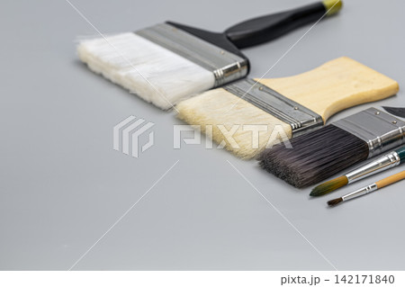 Various sizes of professional artist paintbrushes, including wide flat background wash brushes and fine detail watercolor tools, laid out diagonally on a minimal grey tabletop with negative space. Various sizes of professional artist paintbrushes, including wide flat background wash brushes and fine detail watercolor tools, laid out diagonally on a minimal grey tabletop with negative space. 142171840
