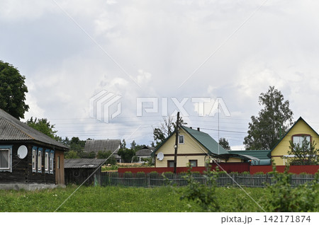 Wooden country houses stand in quiet green village under overcast summer sky. Wooden country houses stand in quiet green village under overcast summer sky. 142171874