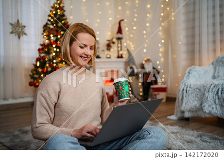 Woman enjoying laptop and coffee during Christmas holiday 142172020