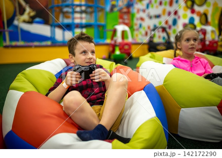 Children holding controllers and playing video games in bean bag chairs Children holding controllers and playing video games in bean bag chairs 142172290