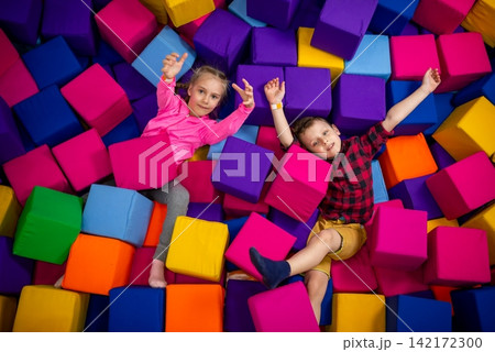 Joyful kids lying down in a pool of soft colorful foam cubes Joyful kids lying down in a pool of soft colorful foam cubes 142172300