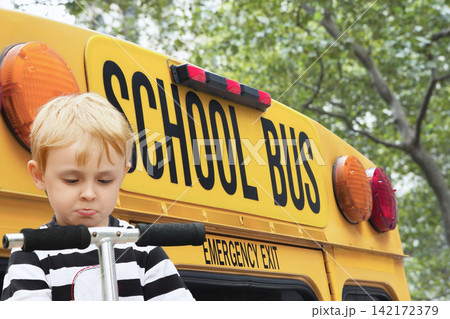 Sad boy on a scooter front of a school bus. 142172379