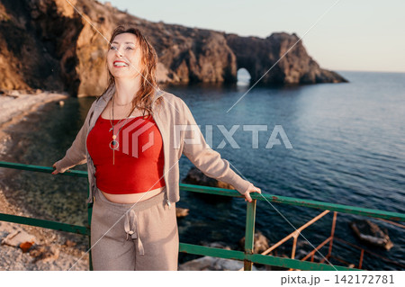 Woman sea sunset standing at coastal viewpoint overlooking rocky cliffs during golden hour for travel concept Woman sea sunset standing at coastal viewpoint overlooking rocky cliffs during golden hour for travel concept 142172781