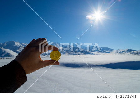 Hand Holds Bitcoin Coin in Snowy Kyrgyzstan Landscape 142172841
