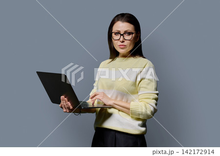 Confident mature woman in glasses holding laptop looking at camera portrait 142172914