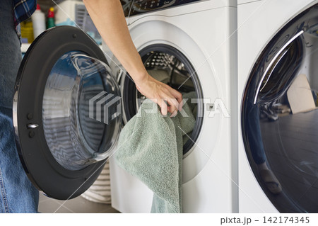 Woman puts towel into open washing machine in home laundry area 142174345