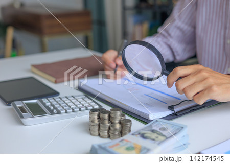 A person using magnifying glass to conduct a financial audit and bookkeeping review. financial analysis and forensic accounting to prevents leaks and invoicing errors. A person using magnifying glass to conduct a financial audit and bookkeeping review. financial analysis and forensic accounting to prevents leaks and invoicing errors. 142174545