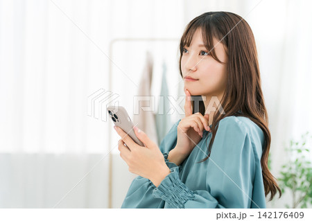 オフィス・仕事場でスマホ・スマートフォンを使う若いアジア人ビジネスウーマン 142176409