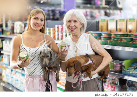 Senior woman and girl chooses dog food for dachshund in pet store. 142177175