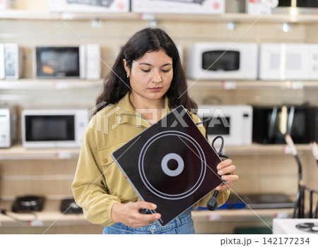 Young woman choosing portable electric cooktop at household appliances store Young woman choosing portable electric cooktop at household appliances store 142177234
