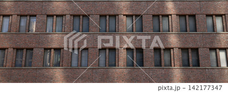 Brick facade displays a series of evenly spaced windows in urban setting Brick facade displays a series of evenly spaced windows in urban setting 142177347