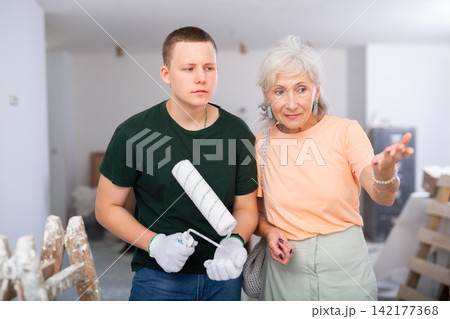 Guy helps his grandmother to renovate the room during holidays. Grandma points with her finger what to do Guy helps his grandmother to renovate the room during holidays. Grandma points with her finger what to do 142177368