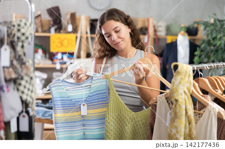 Young woman chooses a set of clothes for the summer. Visitor to the boutique examines new summer collection of clothes Young woman chooses a set of clothes for the summer. Visitor to the boutique examines new summer collection of clothes 142177436