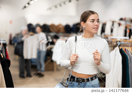 Young girl watching excitedly large stock of clothes in clothing store Young girl watching excitedly large stock of clothes in clothing store 142177686