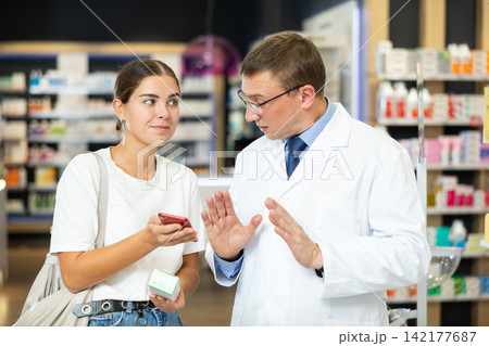 Young girl showing to male pharmacist QR-code of product on her smartphone 142177687