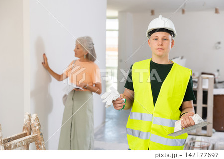 Mature woman checks the construction work performed by a fifteen-year-old worker 142177697