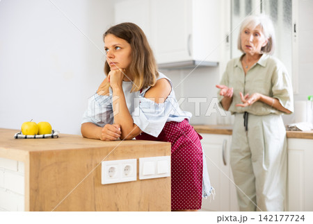 Upset girl at home kitchen while worried elderly mother reprimanding her. Family conflicts concept 142177724