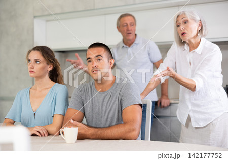 Portrait of an offended married couple in home kitchen, which mature family members reprimand. Family conflict Portrait of an offended married couple in home kitchen, which mature family members reprimand. Family conflict 142177752