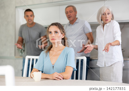 Domestic quarrel - offended young woman sits at table while parents and young husband yell at her Domestic quarrel - offended young woman sits at table while parents and young husband yell at her 142177831