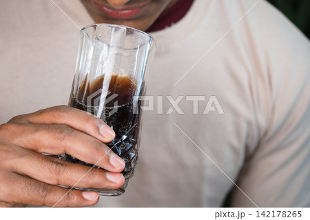 Person holding a glass of soft drinks indoors Person holding a glass of soft drinks indoors 142178265