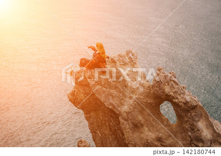 Woman hiker sunset young redhead adventurer sits on a coastal rock formation taking a photo of the sea at golden hour Woman hiker sunset young redhead adventurer sits on a coastal rock formation taking a photo of the sea at golden hour 142180744