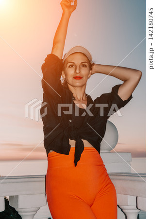 Vibrant young woman posing outdoors on a white balcony during a scenic sunset Vibrant young woman posing outdoors on a white balcony during a scenic sunset 142180745
