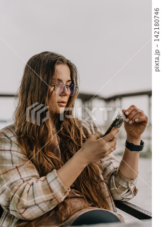 Woman smartphone outdoors young female in plaid jacket checking messages on her mobile device while sitting on a terrace Woman smartphone outdoors young female in plaid jacket checking messages on her mobile device while sitting on a terrace 142180746