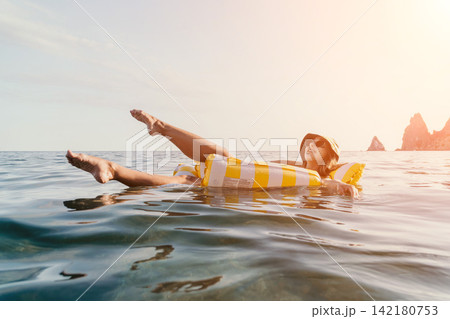 Woman Inflatable Raft Sea Relaxing on a yellow and white inflatable raft in the sea, with rocky cliffs in the background. 142180753